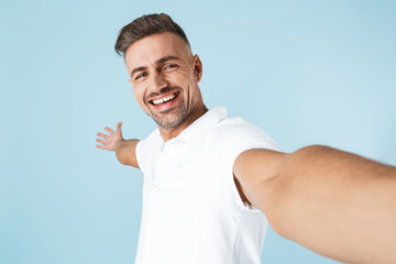 Poster - Emotional adult man posing isolated over blue wall background take a selfie by camera.