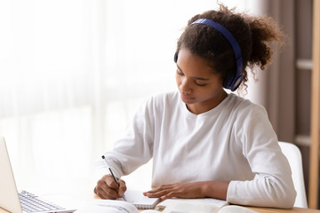 Wall Mural - Serious African American teenage girl wearing headphones, doing homework