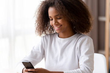 Smiling African American teenage girl using phone, looking at screen