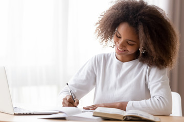 Wall Mural - Smiling African American teen girl preparing school homework, using laptop