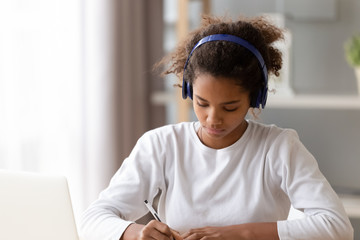 Wall Mural - African American teenage girl wearing headphones, doing homework