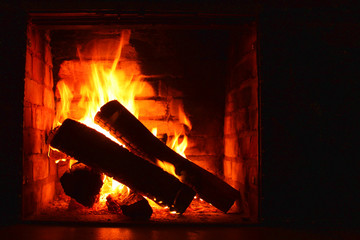 Photo with beautiful brick fireplace with firewood burning in fire and with place for advertising or greeting inscription on dark background