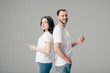 © LIGHTFIELD STUDIOS - young smiling man and woman in white t-shirts standing back to back and using smartphones isolated on grey