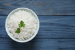Bowl of cooked rice with parsley on wooden background, top view. Space for text