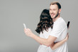 © LIGHTFIELD STUDIOS - young couple in white t-shirts hugging while using smartphones on grey background