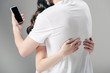 © LIGHTFIELD STUDIOS - cropped view of woman embracing man using smartphone on grey background