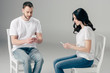 © LIGHTFIELD STUDIOS - focused man and woman in white t-shirts and blue jeans sitting on chairs and using smartphones on grey background