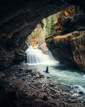 Person Standing On Cave Facing Waterfalls