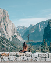 Woman Sitting On Concrete Fence Facing Mountains