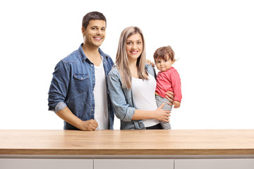 Sticker - Young family of a mother, father and a baby girl posing behind a wooden counter