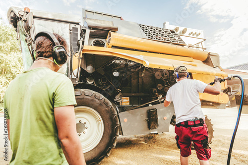 Cuadros en Lienzo The mechanics repair the yellow and green combine harvester in the farm yard