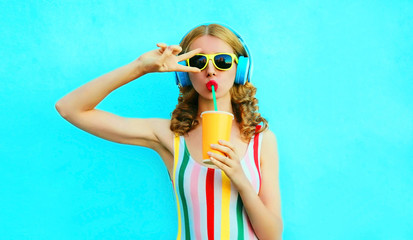 portrait cool girl drinking fruit juice listening to music in wireless headphones on colorful blue b