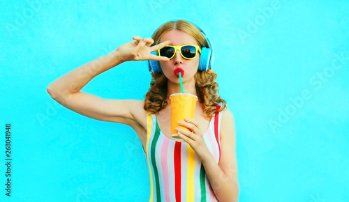 Fotografía Portrait cool girl drinking fruit juice listening to music in wireless headphone