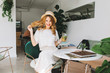 © Look! - Cheerful girl in trendy vintage hat playing with blonde hair and laughing relaxing in cafe. Excited fair-haired lady in white outfit drinking cocktail and having fun while chilling in cozy restaurant.