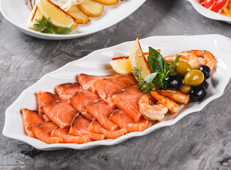 Seafood platter with salmon slice, shrimp, slices fish fillet, decorated with olives and lemon in plate over rustic background. Mediterranean appetizers, closeup.