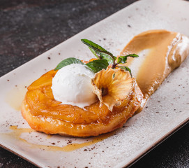 Wall Mural - Breakfast with delicious apple strudel with pineapple, jam, ice cream garnished with mint and powdered sugar on light plate over dark background. Puff pastries, dessert, bakery. Top view, flat lay.