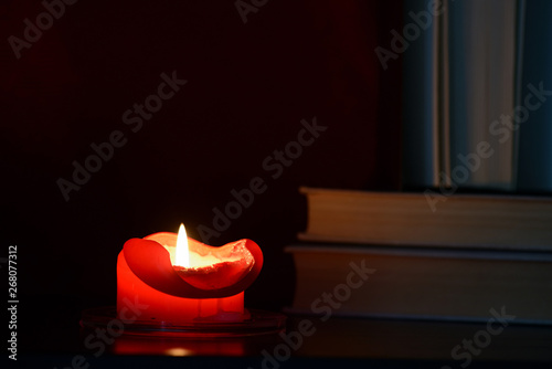Obraz Dibond Red burning candle and old books in the dark close up