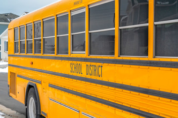 Wall Mural - Close up of a yellow school bus on a snowy road against homes and cloudy sky