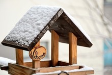 Wooden Bird Feeder With "Welcome" Sign. Homemade Birds Feeder Covered With Snow At Winter Time,  Attached To A Metal Handrail On The Balcony