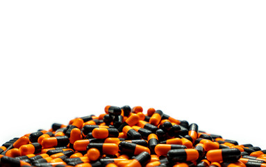 Canvas Print - Closeup pile of orange-black capsule pills on white background. Vitamins and supplements. Pharmaceutical industry. Global healthcare concept. Capsule pills production. Drug over use in health system.