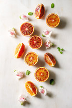 Group Of Fresh Organic Sicilian Blood Oranges Sliced And Whole, Edible Flowers, Mint Leaves Over White Marble Background. Flat Lay, Space