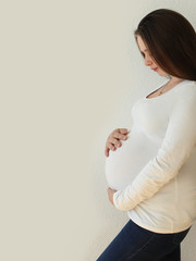 Poster - pregnant girl with a big belly in white clothes is standing, supports her belly, close-up