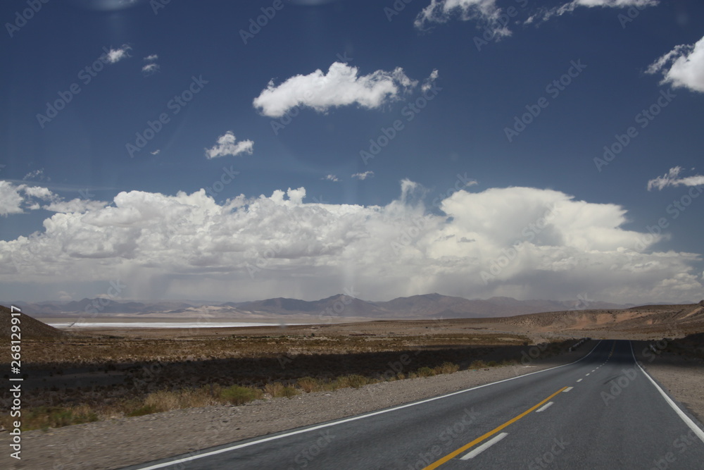 asfaltowa droga prowadząca do wielkiej solnej równiny w argentynie z andami i niebem w tle - obrazy, fototapety, plakaty 