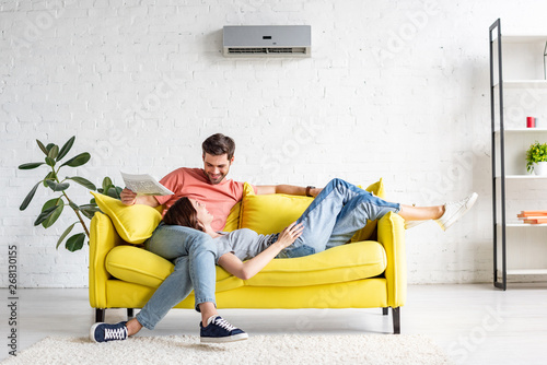 Fotografía happy man with smiling girlfriend relaxing on yellow sofa under air conditioner