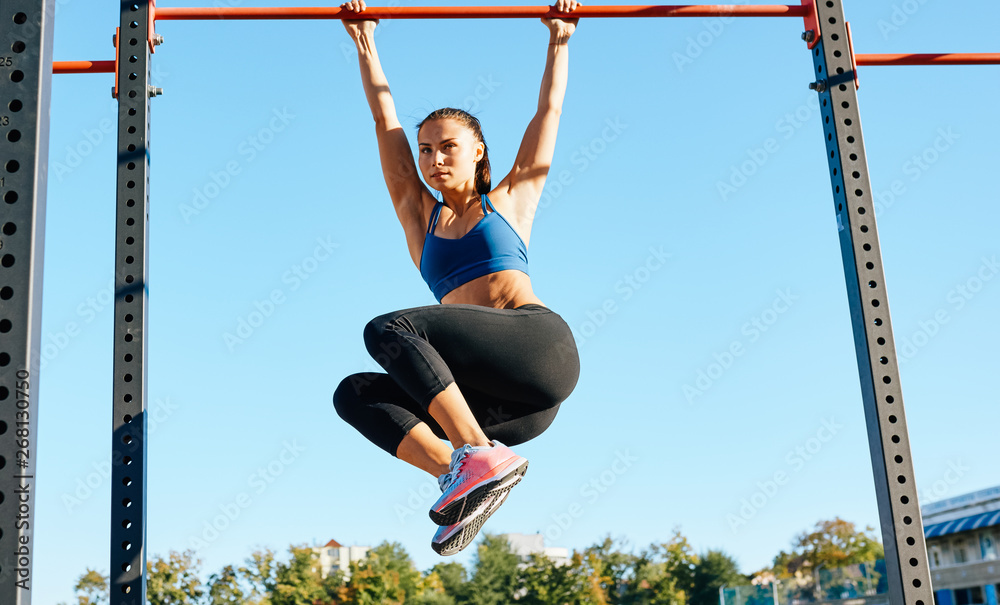 Fit young female doing pull ups exercises on crossbar outdoors. Athlete ...