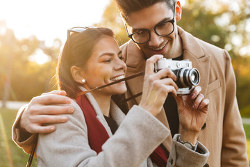 Sticker - Portrait of smiling couple taking photo on retro camera while walking in autumn park