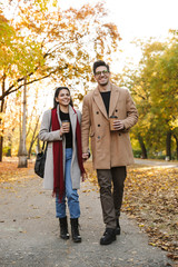 Canvas Print - Portrait of casual couple drinking takeaway coffee from paper cups while walking in autumn park