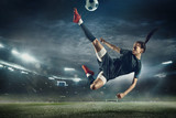 Fototapeta Sport - Young female soccer or football player with long hair in sportwear and boots kicking ball for the goal in jump at the stadium. Concept of healthy lifestyle, professional sport, hobby, motion, movement