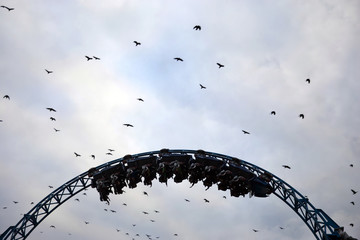 Wall Mural - Silhouette of people having fun on a roller-coaster in an amusement park at sunset. Adrenalin concept.