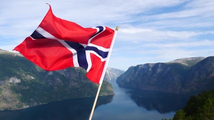 Wall Mural - Norwegian flag waving in slow motion against fjord Aurlandsfjord landscape. View from Stegastein viewpoint. National tourist route Aurlandsfjellet