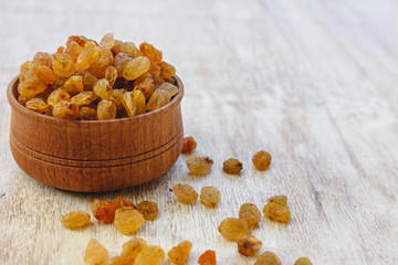 Wall Mural - Light yellow raisins in a wooden bowl on a light white background. Close-up. Isolated.