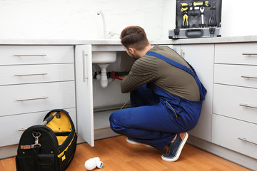 Wall Mural - Male plumber in uniform repairing kitchen sink