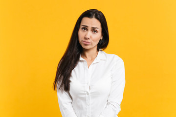 Portrait of upset offended young woman in white casual shirt standing and looking camera isolated on bright yellow orange wall background in studio. People lifestyle concept. Mock up copy space.