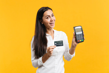 Cheerful young woman holding wireless modern bank payment terminal to process and acquire credit card payments isolated on yellow orange wall background. People lifestyle concept. Mock up copy space.