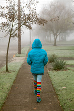 Girl Wearing Rainbow Socks Walks Down A Sidewalk On A Foggy Morning
