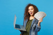© ViDi Studio - Young african american girl teen student in denim clothes, backpack hold pc, fan of cash money isolated on blue wall background. Education in high school university college concept. Mock up copy space