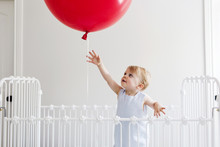 Girl In Crib Trying To Touch Red Balloon
