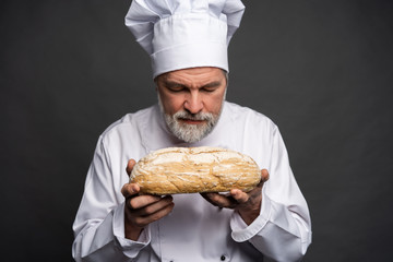 Wall Mural - Portrait of a male chef cook smelling fresh bread against black background.