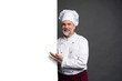 © opolja - Portrait of a happy mature chef cook showing copyspace on the palms isolated on black background.