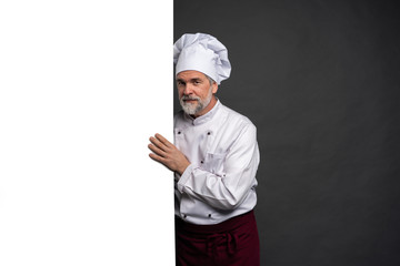 Wall Mural - Portrait of a happy mature chef cook showing copyspace on the palms isolated on black background.