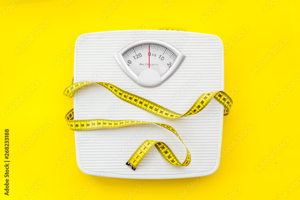 bathroom scales and measuring tape for weight loss concept on yellow background top view - obrazy, fototapety, plakaty 