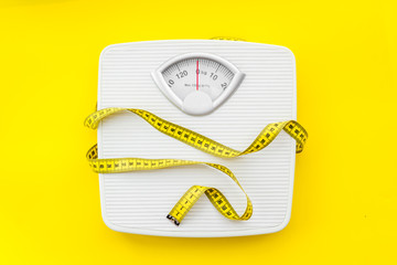 bathroom scales and measuring tape for weight loss concept on yellow background top view