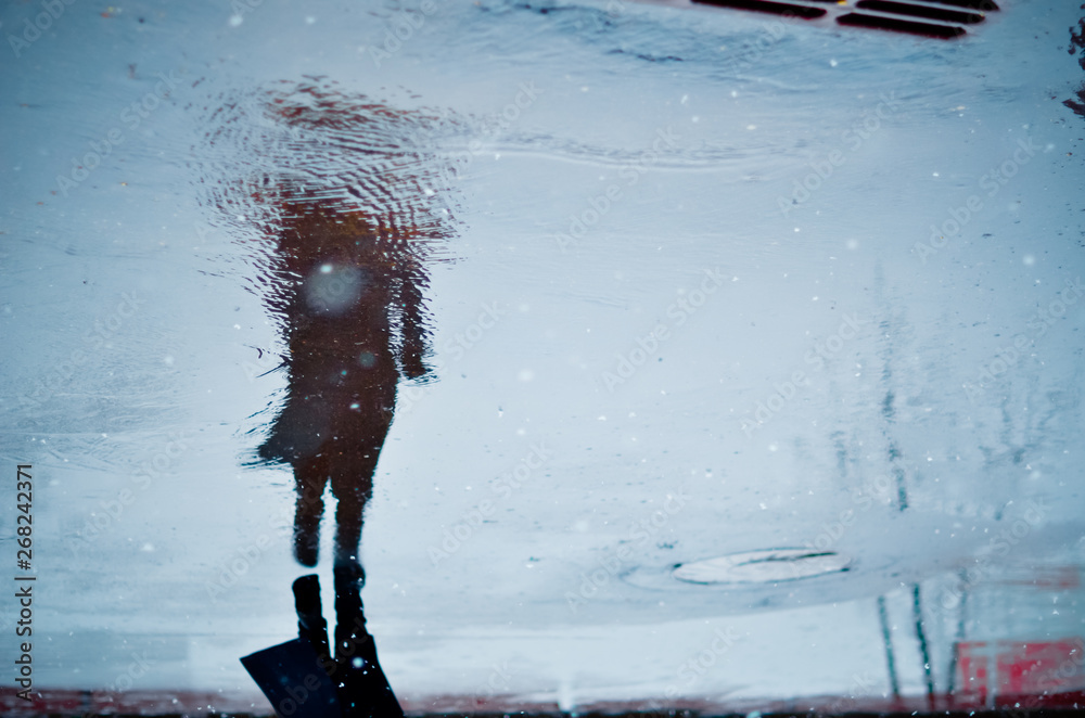 Blurry reflection in a puddle of alone walking person on wet city street during rain and snow. Mood concept - obrazy, fototapety, plakaty 