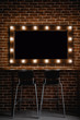 A makeup mirror with light bulbs  and wooden frame on a brown brick wall background with black space for text inside 