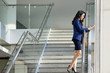 © DragonImages - Young pretty manager standing at stairs of modern office and typing a message on her mobile phone