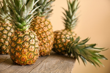 Ripe pineapples on wooden table against color background